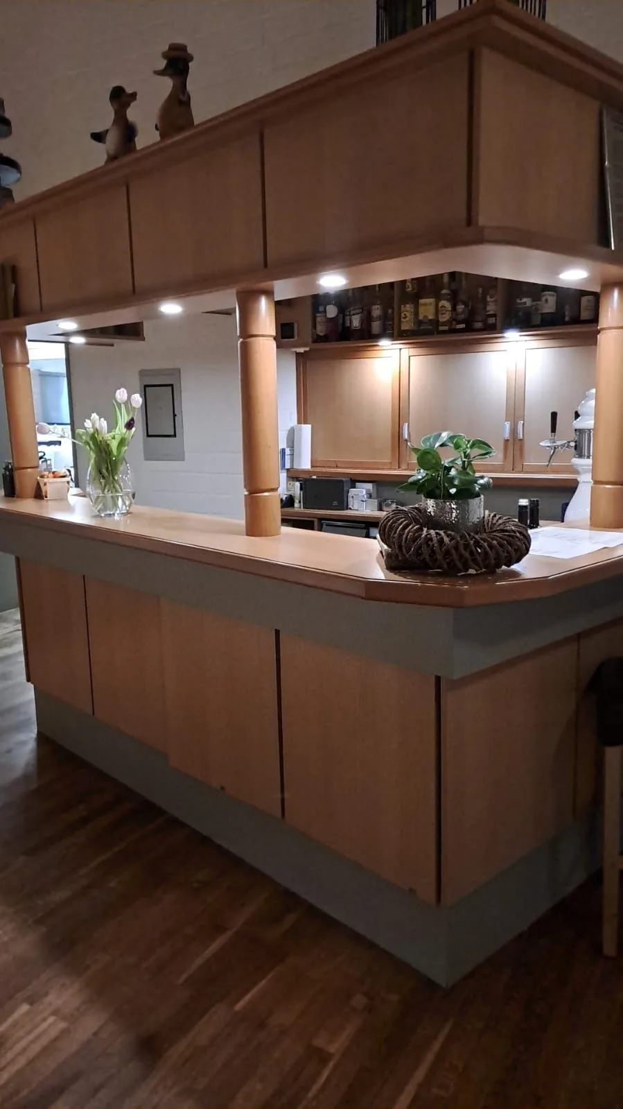 Der Tresen der Gaststube aus hellem Holz, warm beleuchtet, mit Tulpen und einem Napfkuchen auf der Theke