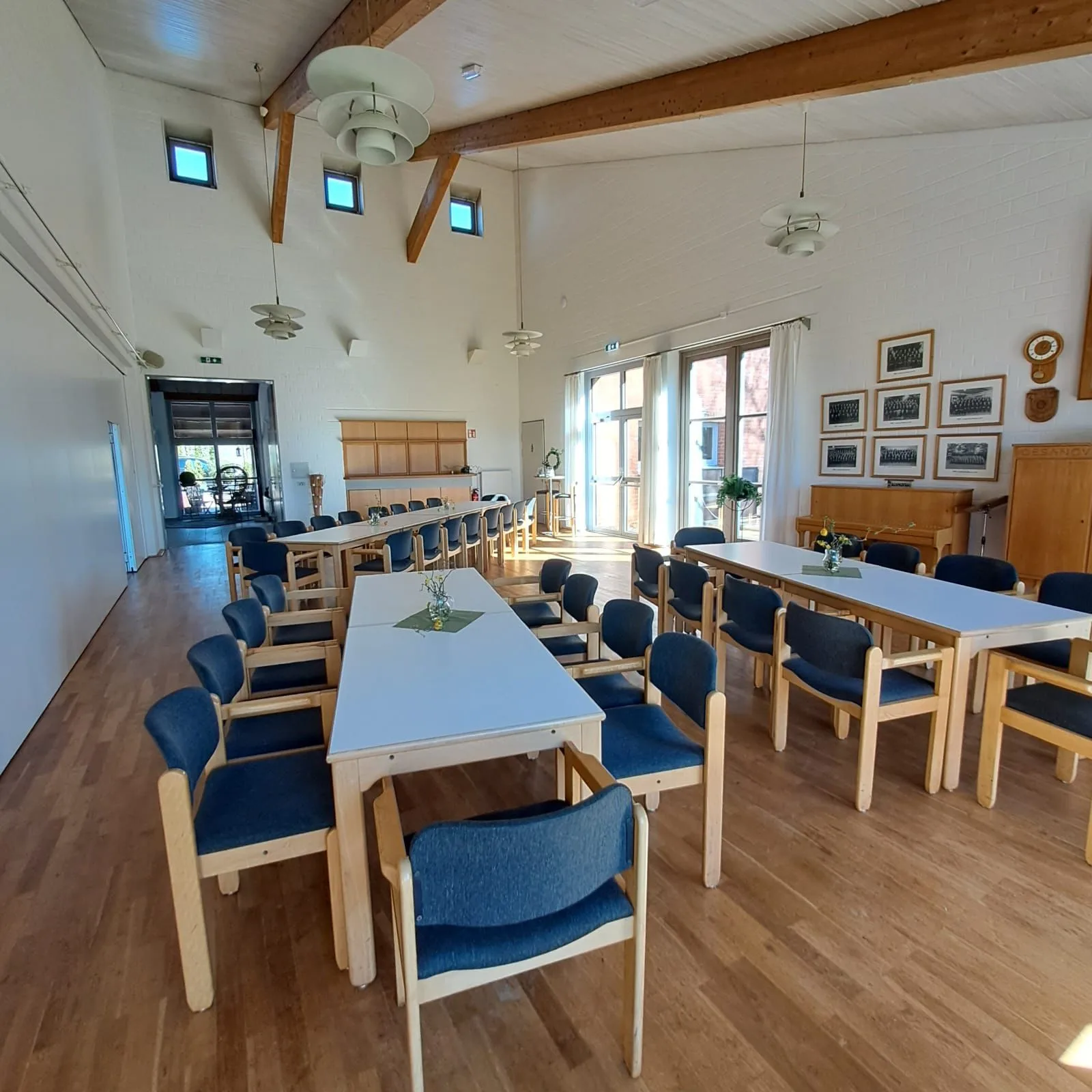 Saal für eine Versammlung gestellt: lange Tische in Reihe, blaue Polsterstühle, Bilderrahmen an der Wand