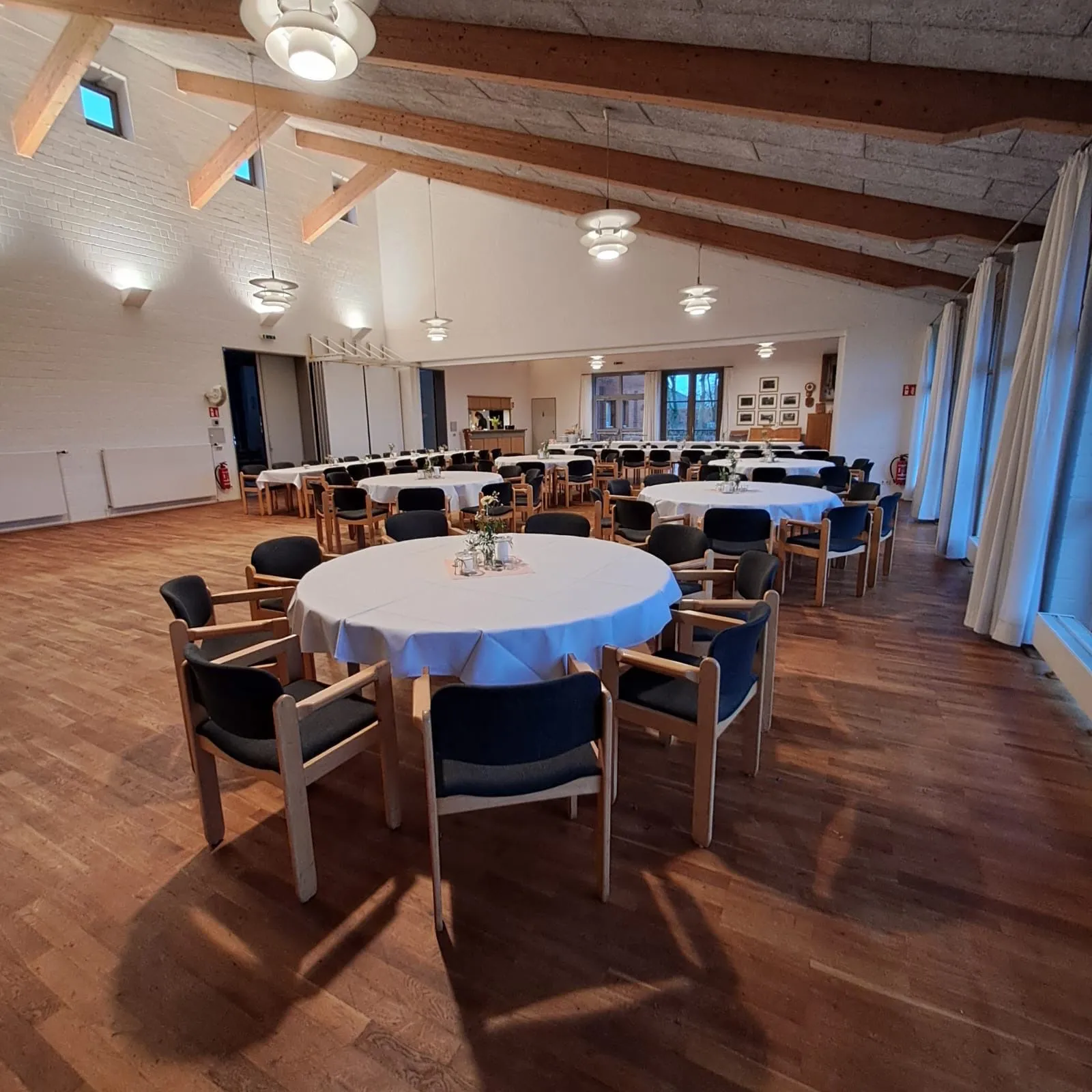 Runde Tafel mit hellblauer Decke im Vordergrund, dahinter der Saal mit langen Tafeln