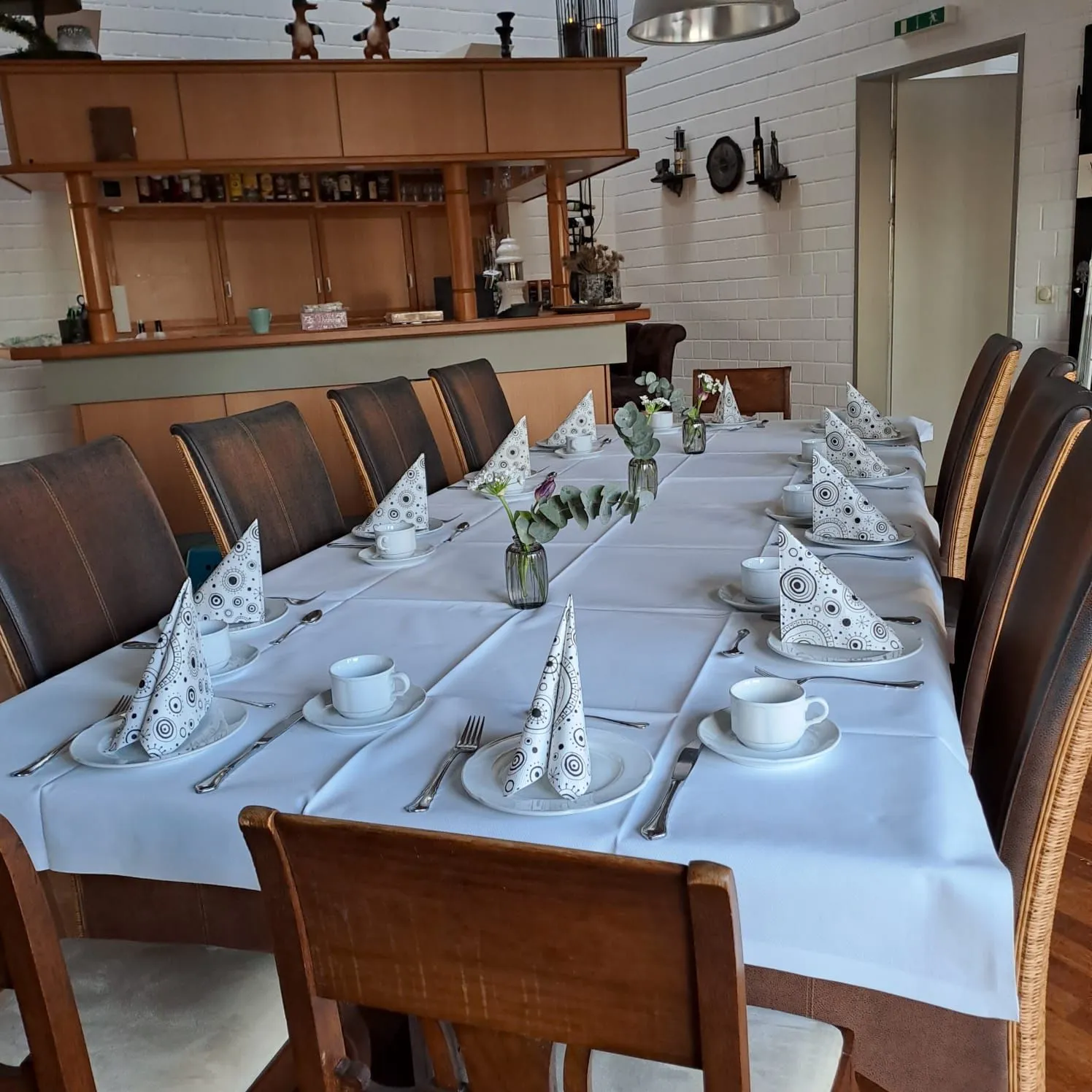 Die Gaststube: Tresen aus hellem Holz, davor eine lange weiß gedeckte Tafel