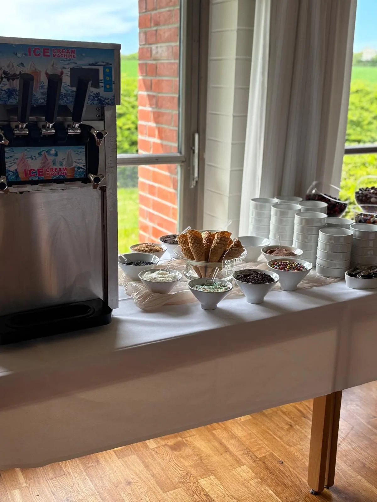 Eismaschine und Dessertbüfett am Fenster, dahinter Backstein und Wiese